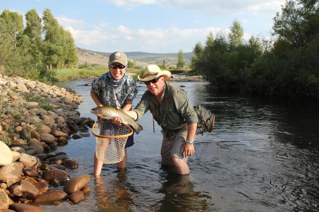 A pair of anglers holding a large trout in a river.